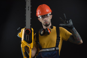 a young man posing on a black background in a work uniform and a construction tool