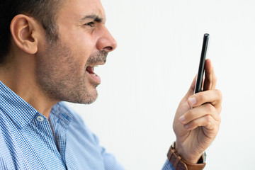 Closeup of angry business man shouting at smartphone. Indignant guy using device. Indignation and technology concept. Isolated side view on white background.
