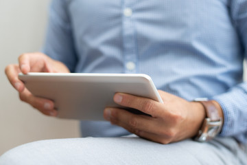 Closeup of business man sitting and using tablet computer. Man browsing on digital device. Technology and communication concept. Cropped front view.