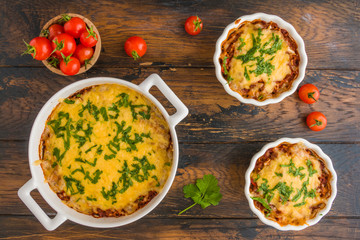 Ground beef baked with tomato, bell pepper, onion and rice and topped with grated cheese and fresh parsley in white baking dishes on wooden rustic table