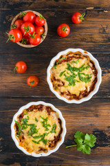 Ground beef baked with tomato, bell pepper, onion and rice and topped with grated cheese and fresh parsley in white baking dishes on wooden rustic table