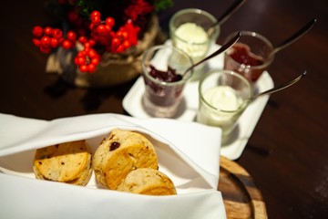 A tasty and delicious set of freshly baked raisin scones with clotted cream and jam for afternoon tea or high tea party in elegant white setting. British way to relaxation and good time. Warm light.