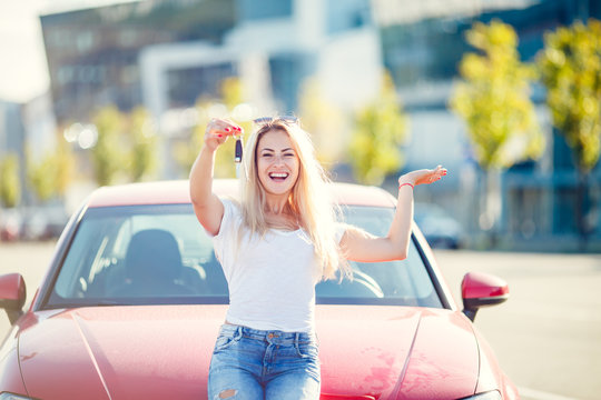 Photo of happy blonde woman with keys standing near red car