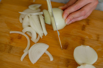 Fototapeta na wymiar Woman with knife cutting onion on wooden cutting board, close-up