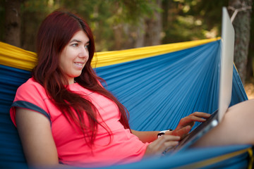 Photo on side of brunette with laptop sitting in hammock