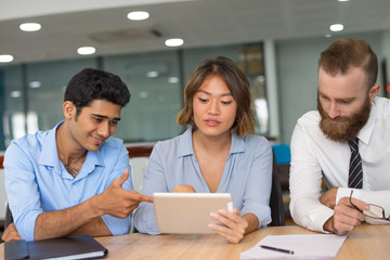 Professionals creating new project. Multiethnic business team using tablet at meeting table. Multiethnic team concept