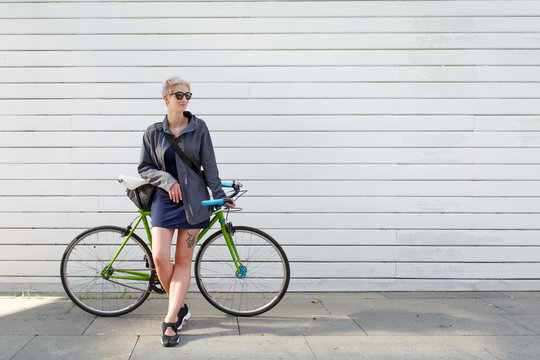 Full-length photo of young blonde with green bike near grey wall