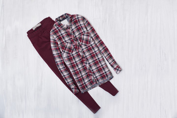 Checkered shirt and burgundy jeans on wooden background. Fashionable concept