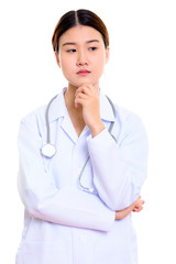 Studio shot of young beautiful Asian woman doctor thinking