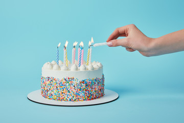 Partial view of woman lighting candles on birthday cake on blue background
