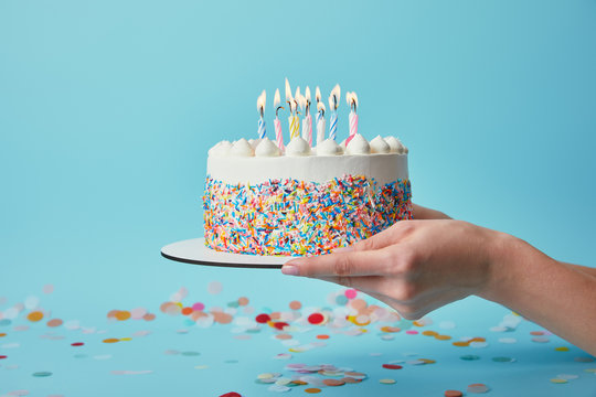 Partial view of woman holding birthday cake with candles on blue background with confetti