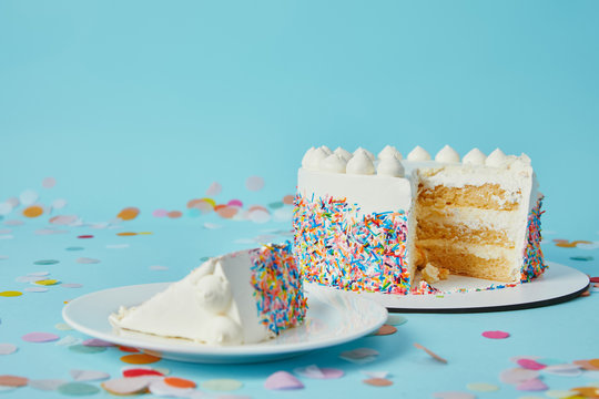 Slice of cake with cut cake on blue background with confetti