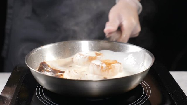 Cooking in restaurant professional cooker in gloves stiring frying pan with scallops boiling in cream sauce. Slow motion. hd