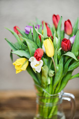 Flower background: bouquet of colorful tulips in a glass vase on a natural wooden background, postcard, mocap for mother's day greetings, international women's day