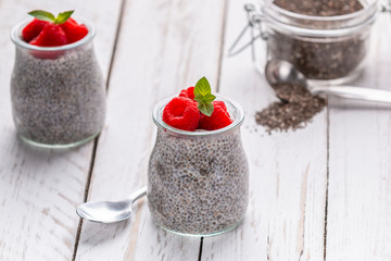 Closeup of served glass jars filled with sweet pudding of chia seeds and garnished with fresh raspberry and mint