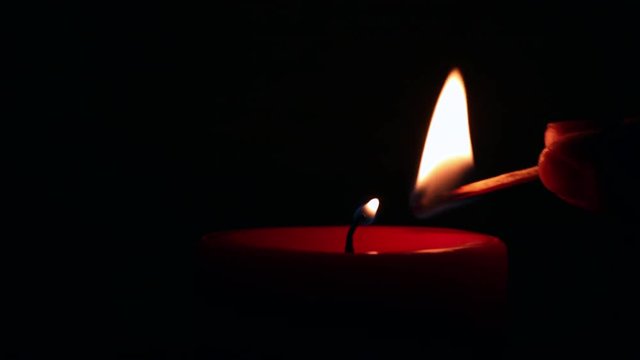 Close up firing a wax red candle with a match