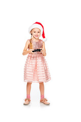 happy little child in santa hat playing video game and looking at camera isolated on white