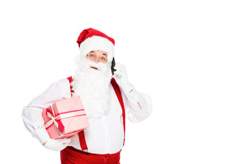 Fototapeta na wymiar emotional santa claus in suspenders holding gift box and talking by phone isolated on white