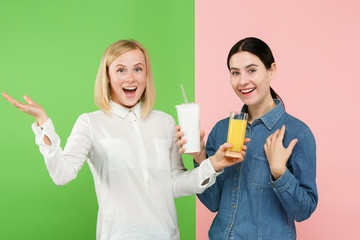 Diet. Dieting concept. Healthy useful food. Beautiful young women choosing between fruit orange juice and unhelathy carbonated sweet drink from fast food at studio. Human emotions and comparison