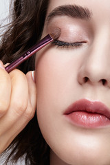 Make-up artist apply beauty makeup on the eyelids of a beautiful girl. Visagist with makeup brush in hand