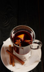 mulled wine on  white plate on black wooden table, cinnamon sticks and orange, top view