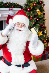 santa claus holding credit card and talking by smartphone