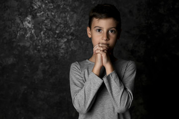 Little boy praying on dark background