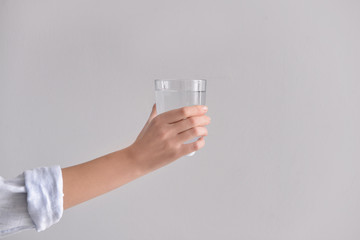Female hand with glass of fresh water on light background