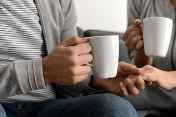 Young couple with cups of tea holding hands at home