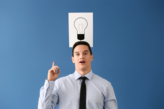 Young businessman and paper sheet with drawn light bulb as symbol of idea on color background