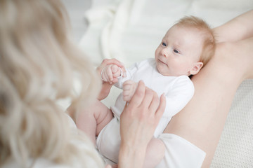 Young mother holding her newborn child.Woman and new born boy relax in a white bedroom.A young mother gently holds her newborn son in her arms.Family at home.Young mother playing whith her newborn son