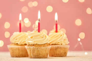 Delicious birthday cupcakes with burning candles against blurred lights