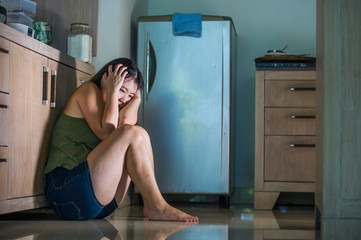 young scared and desperate Asian Japanese woman crying helpless at home kitchen floor suffering domestic violence and sexual abuse victim of jealous husband