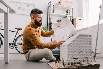 smiling bearded adult male architect working on construction project with house model in office