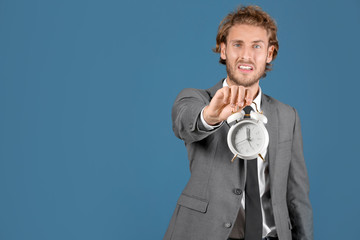 Naklejka premium Stressed businessman holding alarm clock, time management pressure, deadline urgency, business challenges, corporate stress