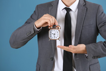 Young businessman with alarm clock on blue background
