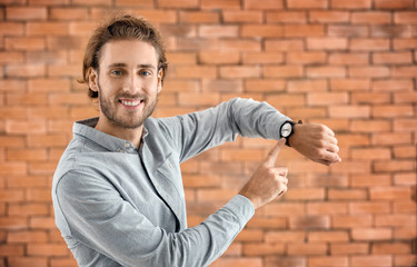 Young man pointing at his watch on brick background
