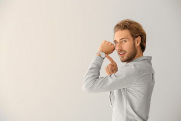 Young man pointing at his watch on light background