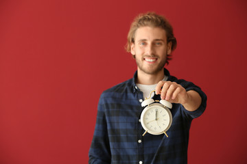 Young man with alarm clock on color background