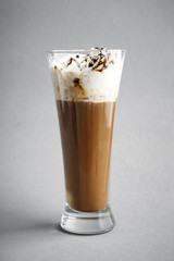 Cold coffee covered with whipped cream and chocolate in glass on grey background