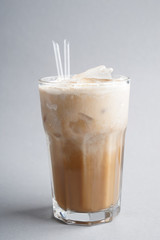 Glass of cold coffee with milk and ice cubes on light background