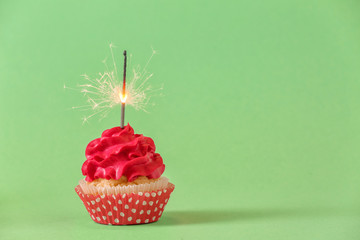 Tasty cupcake with sparkler on color background