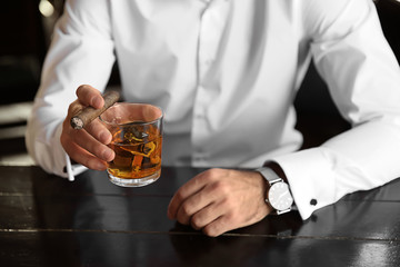 Young man with glass of whiskey and cigar in pub, closeup