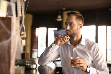 Young man with glass of whiskey and cigar in pub