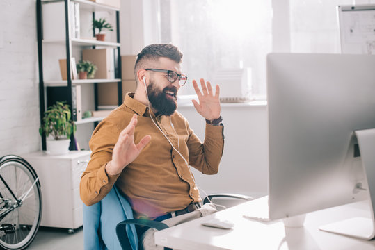 Excited Bearded Adult Businessman In Earphones Sitting At Computer And Listening To Music Desk In Office