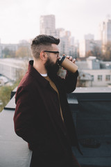 stylish adult man in glasses holding coffee to go on rooftop