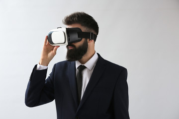 Businessman wearing virtual reality glasses on light background