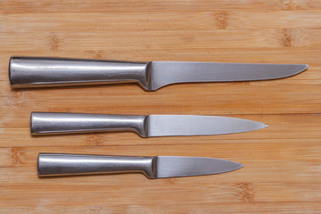 three knives of different sizes lie horizontally on a wooden surface top view