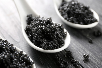 Spoons with delicious black caviar on wooden background