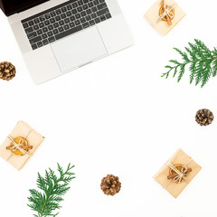 Laptop with Christmas gifts, evergreen branches and pine cones on white background. Holiday office composition. Top view. Flat lay